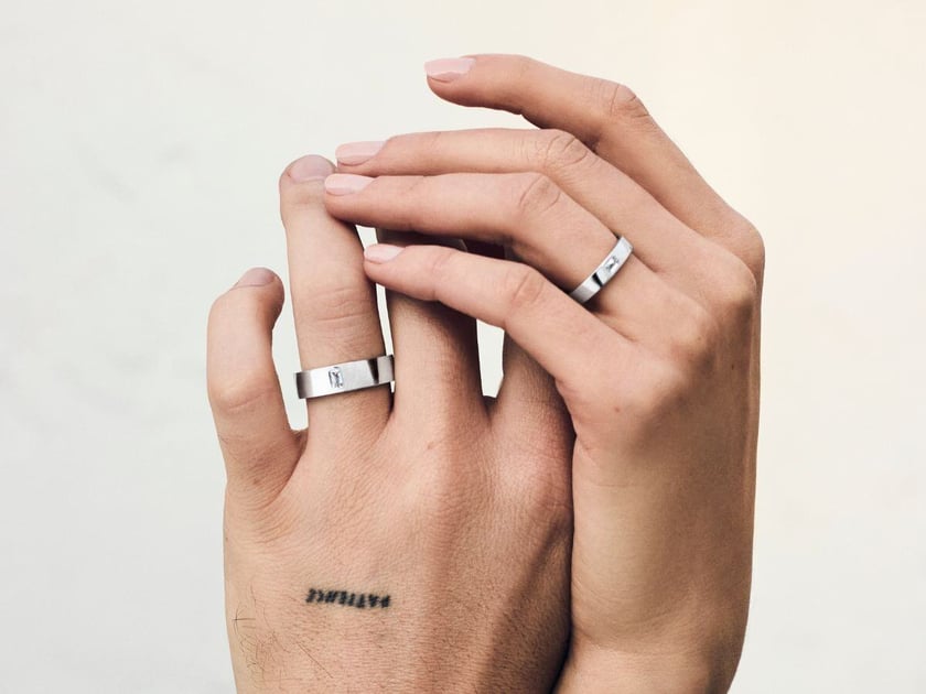 Two holding hands wearing couple's matching wedding bands